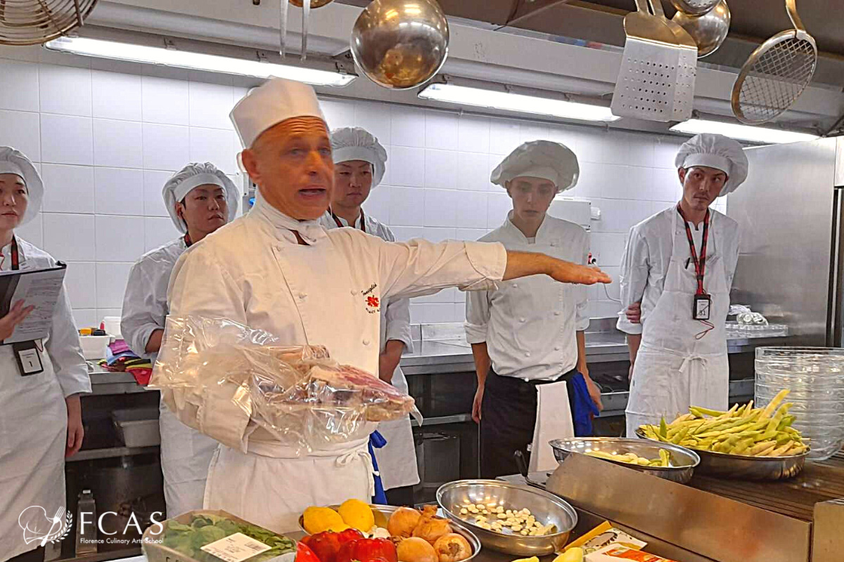 イタリア料理留学　シェフ養成コース授業の様子　食材の肉を手に持って説明する講師